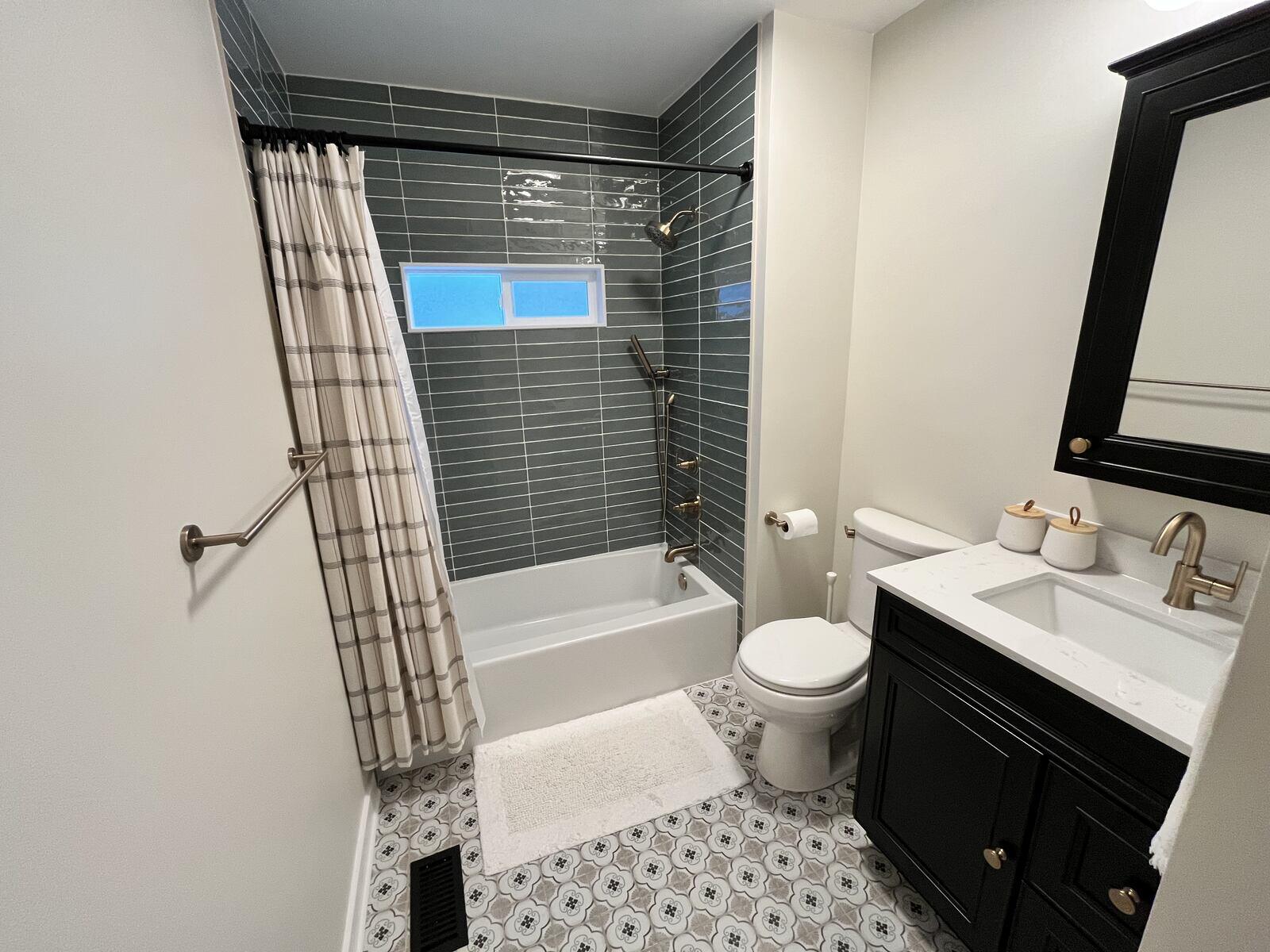 Modern bathroom design with patterned flooring, black cabinetry, and gold fixtures by Clear Contractors in Northwest Indiana