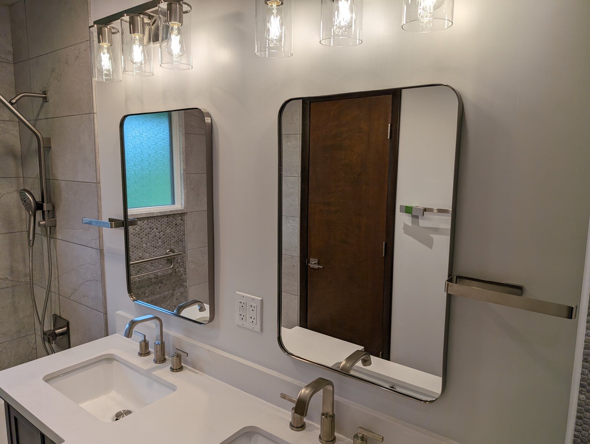 Remodeled bathroom featuring a stylish mirror, lighting fixtures, and a tiled shower by Clear Contractors in Northwest Indiana