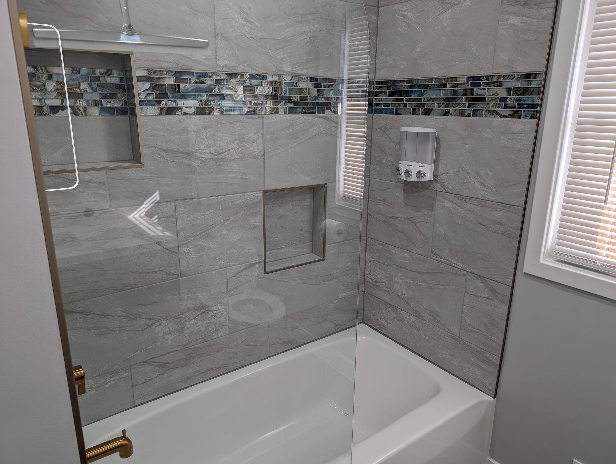 Stylish bathtub with gray marble tile surround and decorative mosaic band by Clear Contractors in Northwest Indiana